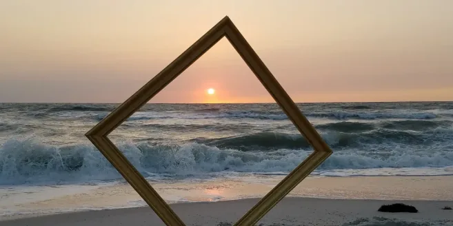 A finished gold moulding held on the beach at sunset, framing the Gulf horizon